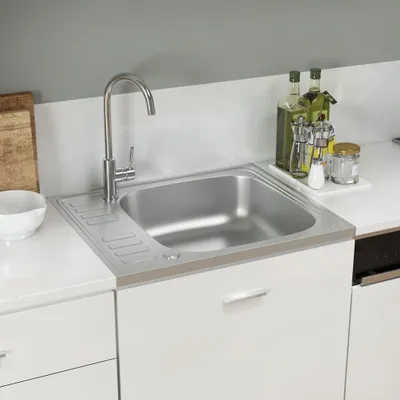 A stainless steel kitchen sink with a faucet and a drying rack is shown on a white countertop.