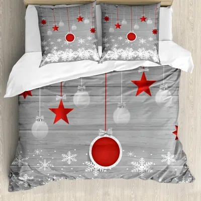 A bedding set with a Christmas theme, featuring red stars, white snowflakes, and hanging ornaments on a gray wooden background.