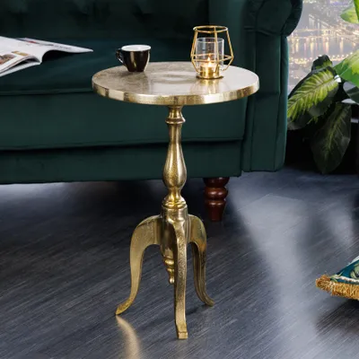 A gold accent table with a candle lantern and a cup on top, placed next to a green sofa.