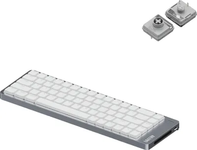 A silver and white low-profile mechanical keyboard is shown from a diagonal angle, with two small, square components with circular elements above it.