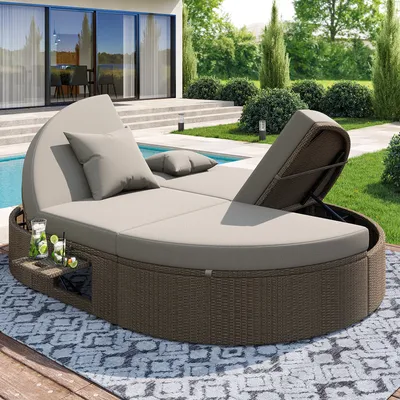 A circular rattan daybed with beige cushions is placed on a patio next to a swimming pool. The background shows a modern house with large glass doors and a manicured garden.