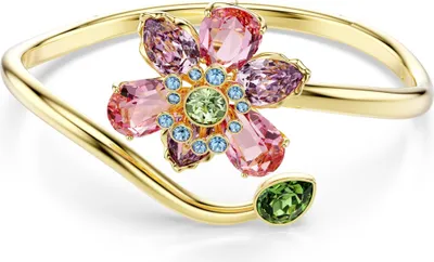 A close-up studio shot of a gold-toned bangle bracelet with a flower design made of colorful crystals.