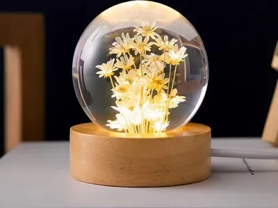 A close-up shot of a decorative crystal ball lamp with dried flowers inside, resting on a wooden base.