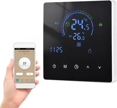 A hand holding a smartphone displaying a thermostat app next to a digital thermostat mounted on a wall.