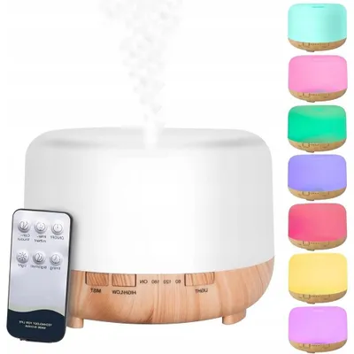 A white ultrasonic humidifier with a wood-tone base, emitting mist, with a remote control in the foreground and a stack of colored lights on the right.