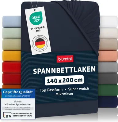 A dark blue fitted sheet is displayed prominently, with a stack of other colored sheets visible on the left and right sides. Several certification labels and product information are also visible.
