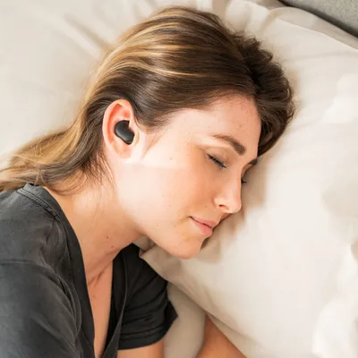 A woman sleeping in bed with earbuds in her ears.