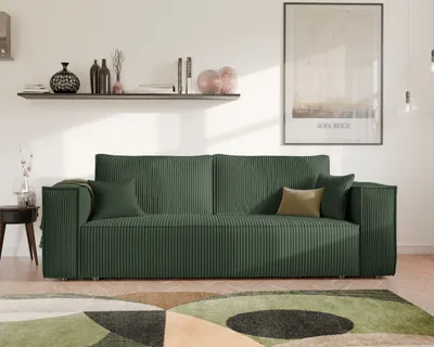 A green sofa is shown in a living room setting with a shelf and a framed picture on the wall.