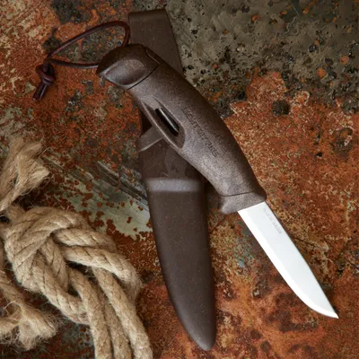 A knife and sheath are placed on a textured, rusty surface next to a coiled rope.