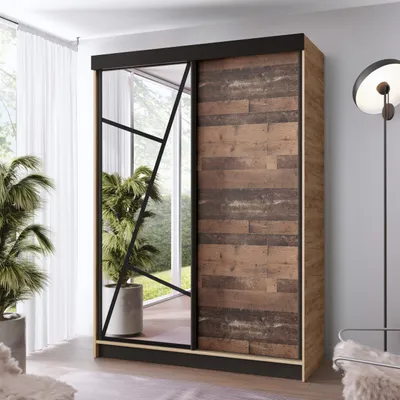 A wardrobe with a mirrored door and a wood-effect door, placed in a room with plants and a lamp.