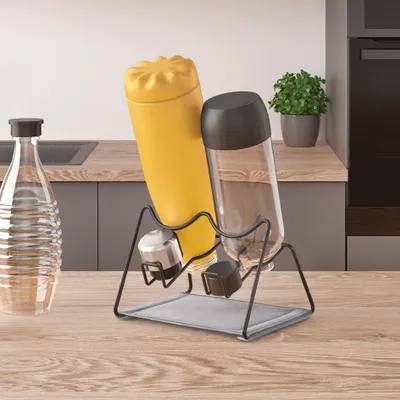 A kitchen counter with a bottle rack holding two bottles and a water bottle, with a plant in the background.