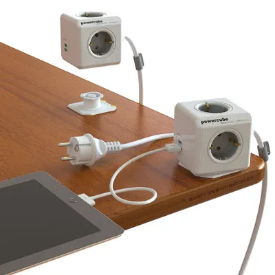 A white PowerCube DuoUSB Extended Grau EU, 4-way socket distributor with 2.1 A USB charging current, White Gray is shown on a wooden desk, plugged into a European power outlet and powering a tablet.