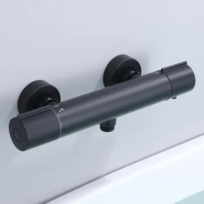A black thermostatic shower faucet mounted on a light gray wall above a white bathtub.
