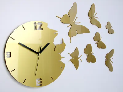A golden clock with butterfly decorations on a white wall.