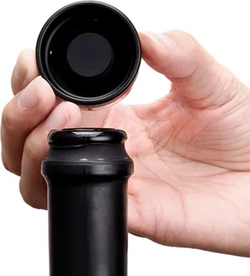 A hand is holding a black bottle cap above a black bottle neck, preparing to seal it.