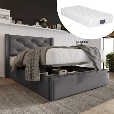 A dark gray upholstered bed frame with a tufted headboard and a mattress is shown in a room setting. The bed has storage drawers underneath, and a blanket is draped over the mattress.
