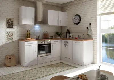 A corner kitchen unit with white cabinets and a wooden countertop, set against a white brick wall.