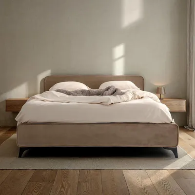 A modern, upholstered bed with a padded headboard is set up in a bedroom with soft lighting.