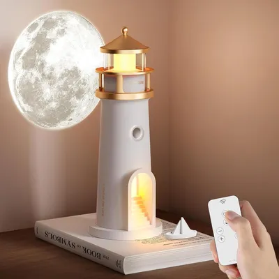 A lighthouse-shaped night light is placed on a book next to a moon projection lamp.