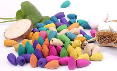 A pile of colorful incense cones scattered on a white surface, with a wooden slice and green leaves in the background.