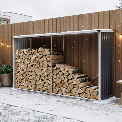 A firewood storage shed filled with logs, set in a snowy outdoor environment with a wooden fence and string lights.