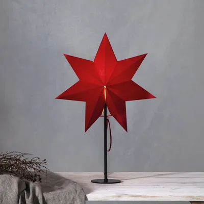 A red star-shaped lamp on a black stand, placed on a table with a grey cloth and dried branches.