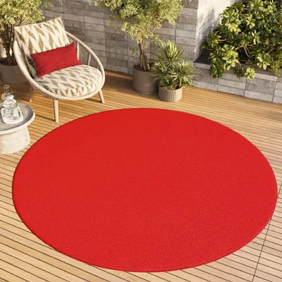 A round red rug on a wooden deck with a chair and plants.