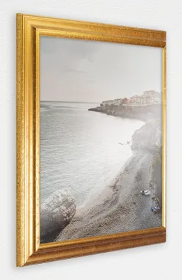 A gold-toned picture frame with a landscape image inside, displayed on a white wall.
