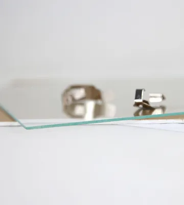 Two small silver-colored accessories, possibly cufflinks or jewelry clasps, are placed on a reflective surface, with a piece of clear glass in the foreground.