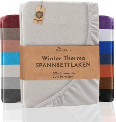 A folded fitted sheet is displayed prominently, with a band of text across the front. Several other fitted sheets in different colors are stacked behind it.