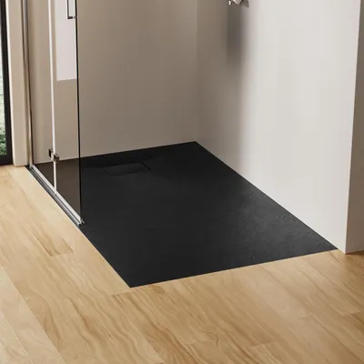 A modern bathroom corner with a black, slate-look shower tray and a glass shower enclosure, set against a white wall and light wood flooring.