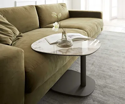 A modern living room scene featuring a green sectional sofa and a small, uniquely shaped side table with a marble-like top.