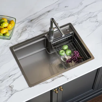 A stainless steel kitchen sink with a faucet, a drying rack with apples and grapes, and a bowl of lemons and limes on a marble countertop.