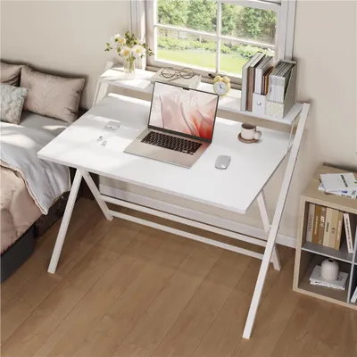 A white folding desk with a laptop, mouse, and coffee cup is set up next to a bed and a window, suggesting a home office or dorm room setup.