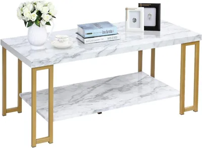 A coffee table with a marble-like top and gold legs, decorated with a vase of flowers, books, and picture frames.