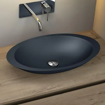 A dark gray oval basin sink with a chrome drain is placed on a light brown wooden countertop. A chrome faucet is mounted on the wall behind the sink.