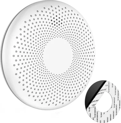 A white, circular smoke and CO detector with a perforated surface is shown on a white background. A circular adhesive pad is also visible in the lower right corner.