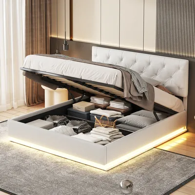 A modern bedroom with a white upholstered bed frame open to reveal storage space underneath, illuminated by LED lighting around the base.