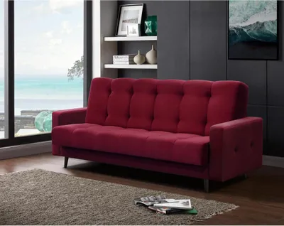 A red sofa is placed in a living room with a large window overlooking the ocean.