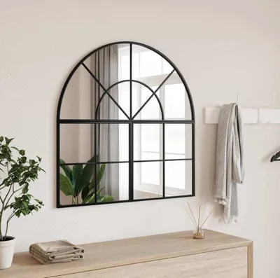 A mirror with a black metal frame, styled on a dresser with a plant and folded towels.