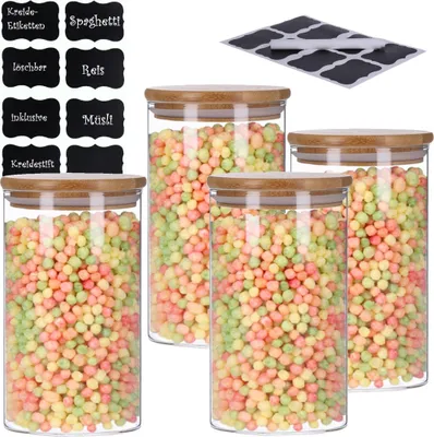 Four glass storage jars filled with colorful cereal or candy, with bamboo lids, and a set of chalk labels in the background.