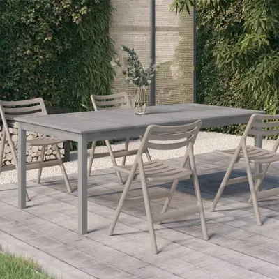 An outdoor dining set with a gray table and beige chairs on a wooden deck, surrounded by lush greenery.
