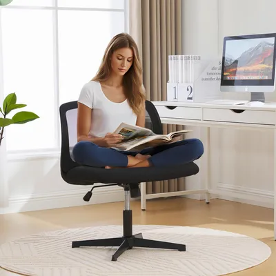 A woman is sitting on a black office chair in a well-lit room, reading a magazine. The chair is in front of a white desk with a computer and a decorative calendar. There is a large window with sheer curtains in the background.