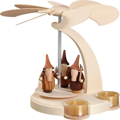 Auf dem Bild ist eine erzgebirgische Bogenpyramide aus Holz zu sehen die mit drei Gnome oder Bergwichteln aus Edelholz dekoriert ist und von Teelichtern umgeben wird während ein Propeller oben angebracht ist