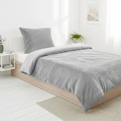 A neatly made bed with gray bedding in a bright room.