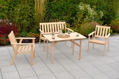 A wooden garden furniture set including a bench, two chairs, and a table, placed on a paved patio with a garden in the background.