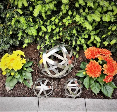 Three decorative metal spheres are placed in a garden bed with flowers and greenery.