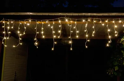 Icicle lights are strung along the edge of a roof at night.