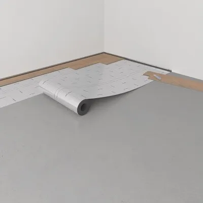 A roll of underlayment material is being unrolled onto a floor, with wood planks visible in the background.