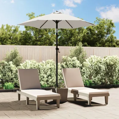 Two lounge chairs and a patio umbrella are set up on a paved patio area with lush green bushes and a wooden fence in the background.